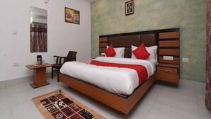 A modern hotel room with a large bed, a wooden headboard, a small desk, and a chair. - OYO 13310 Noida Suites (Noida)