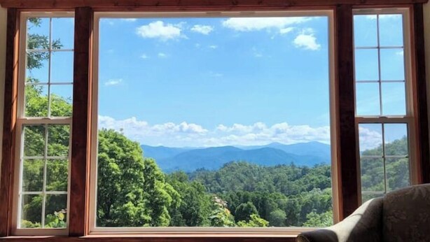 A room with a large window offering a view of a forested mountain range. - Knotty & Nice Cottage Mountain Views, Near Tail of the Dragon, & Fontana Village (Fontana Dam)