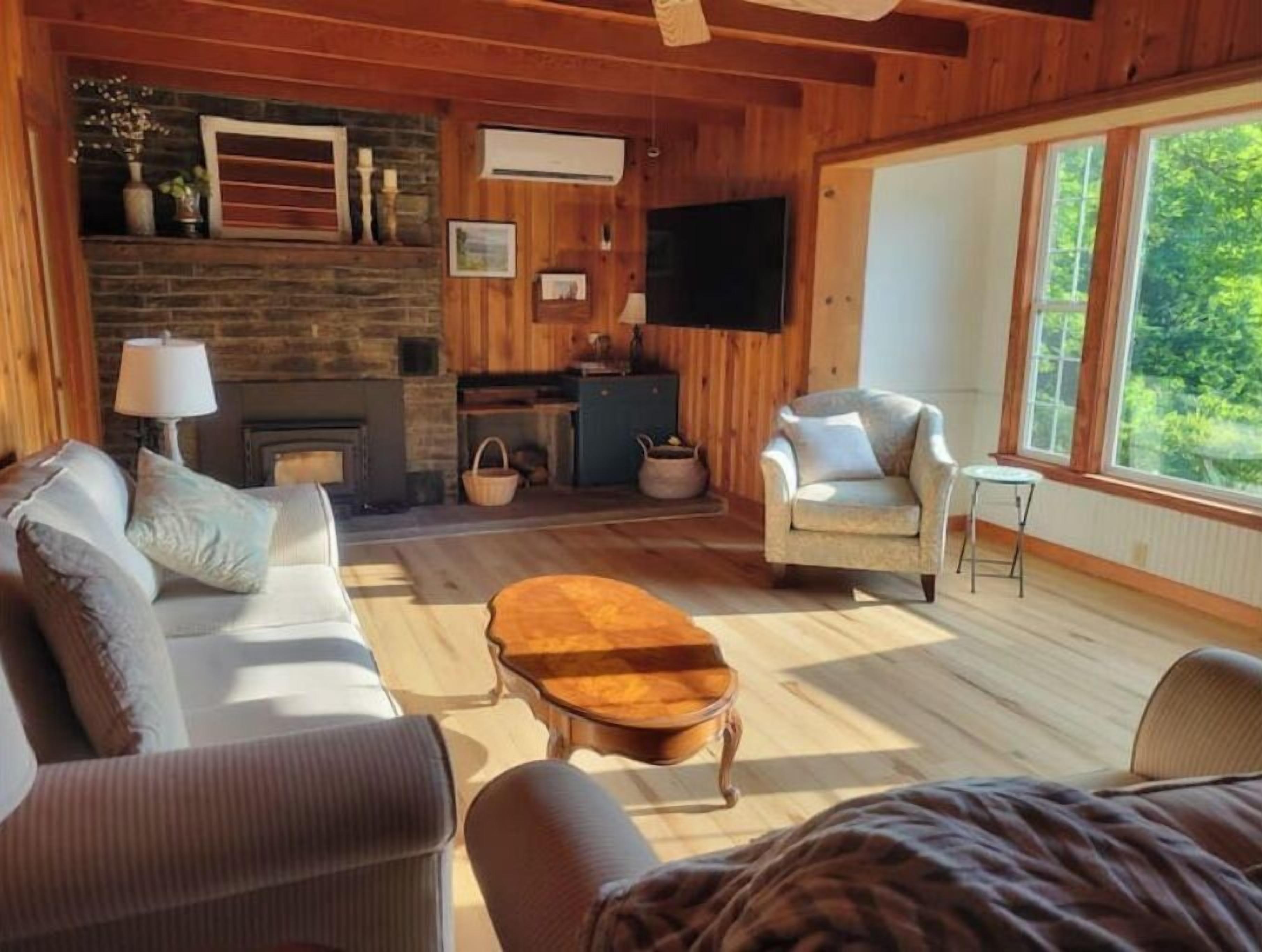 A cozy living room with a fireplace, comfortable seating, and a large window offering a view of the outdoors.