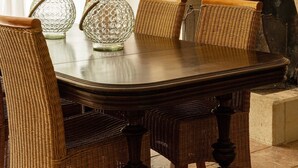 Un comedor con una mesa redonda, sillas de mimbre y jarrones de vidrio decorativos.
