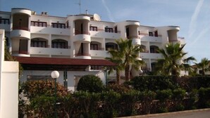 A multi-story hotel with balconies, a central courtyard, and palm trees. - Apartamentos Vista Playa I (Ciutadella de Menorca)