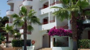 A multi-story hotel with balconies, a swimming pool, and tropical landscaping. - Apartamentos Vista Playa I (Ciutadella de Menorca)