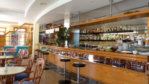 A bar area with wooden bar stools, a counter with various bottles, and a potted plant. - Apartamentos Vista Playa I (Ciutadella de Menorca)