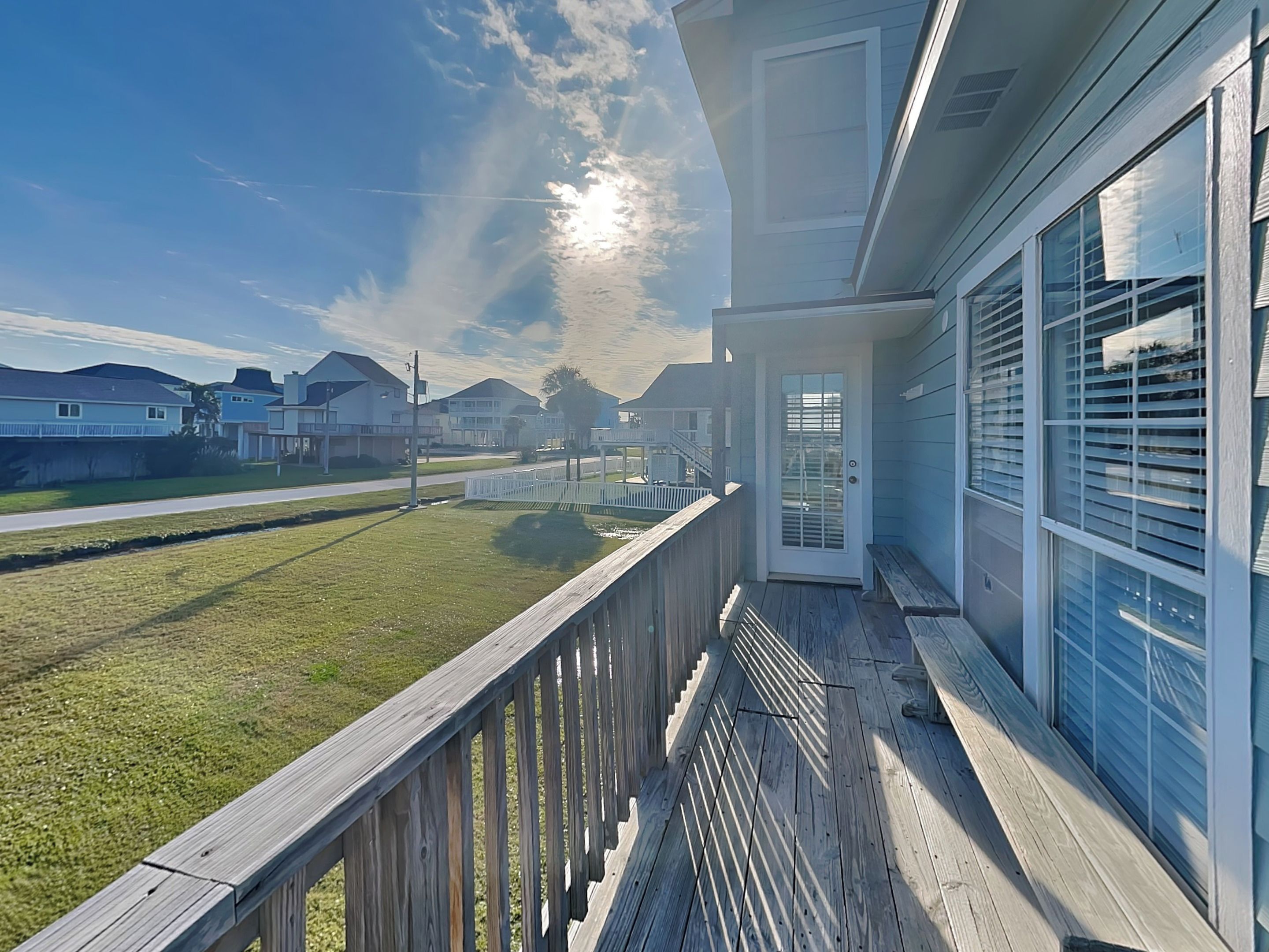 A residential property with a wooden deck, large windows, and a view of neighboring houses.