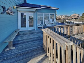 A wooden deck with a covered seating area, a bench, and a fish-shaped decoration on the wall. - ShangriLaLa by Ryson Vacation Rentals (Galveston)