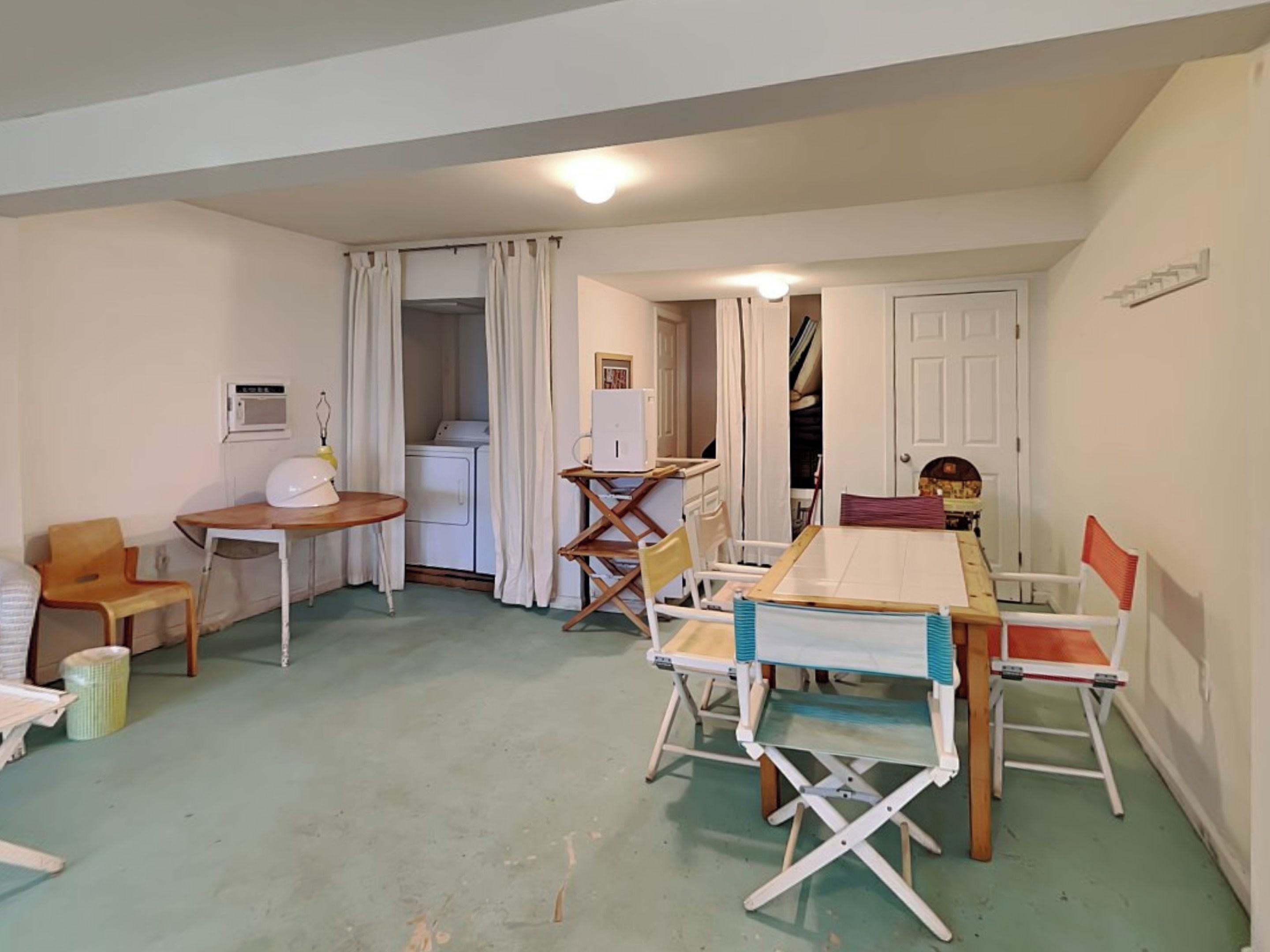 A compact room with a dining table, chairs, a washing machine, and a small kitchen area.