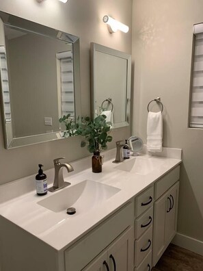 A bathroom with a white sink, two mirrors, a towel ring, and a potted plant. - Game Room/Big TVs King Beds -4 Min to Finley Farms (Ozark)