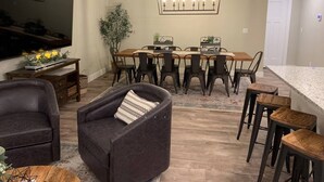 Een moderne woonkamer met een donker leren bank, een houten salontafel en een eethoek met een grote tafel en stoelen.