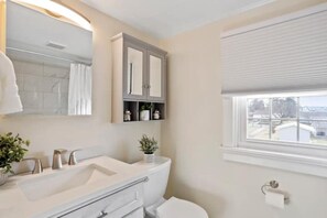 A bathroom with a white sink, a mirror, a cabinet with shelves, a toilet, and a window with blinds. - Patty's Place - Private and Convenient Apartment near Downtown (Frederick)
