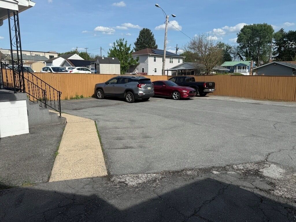 Un parcheggio con diverse auto, una recinzione in legno e case sullo sfondo.
