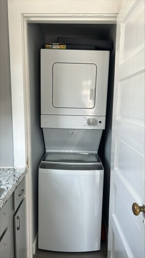A compact laundry room with a stacked washer and dryer, a countertop, and a door with a brass doorknob. - Patty's Place - Private and Convenient Apartment near Downtown (Frederick)