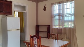 Un coin repas avec une table et des chaises en bois, un réfrigérateur blanc et une fenêtre avec des rideaux.