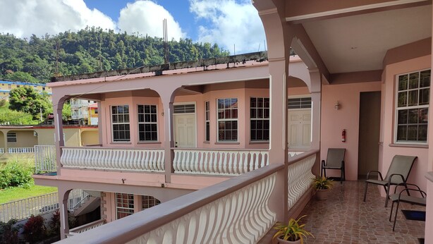 Un bâtiment rose doté d’un balcon, de plantes en pot et d’un extincteur.