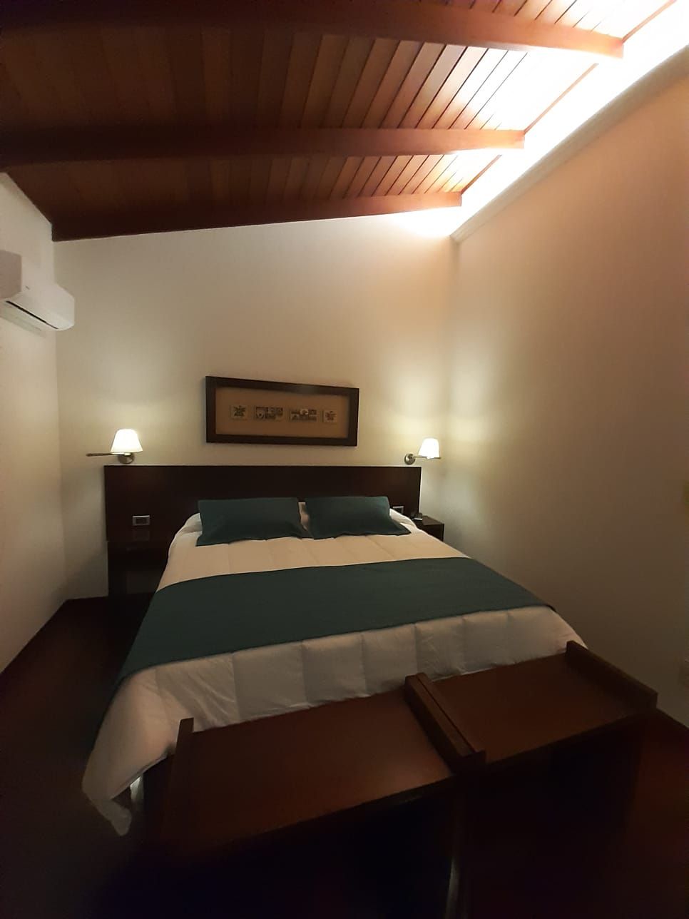 Una camera da letto con un letto, lampade sui comodini, un quadro incorniciato al muro e un soffitto in legno.
