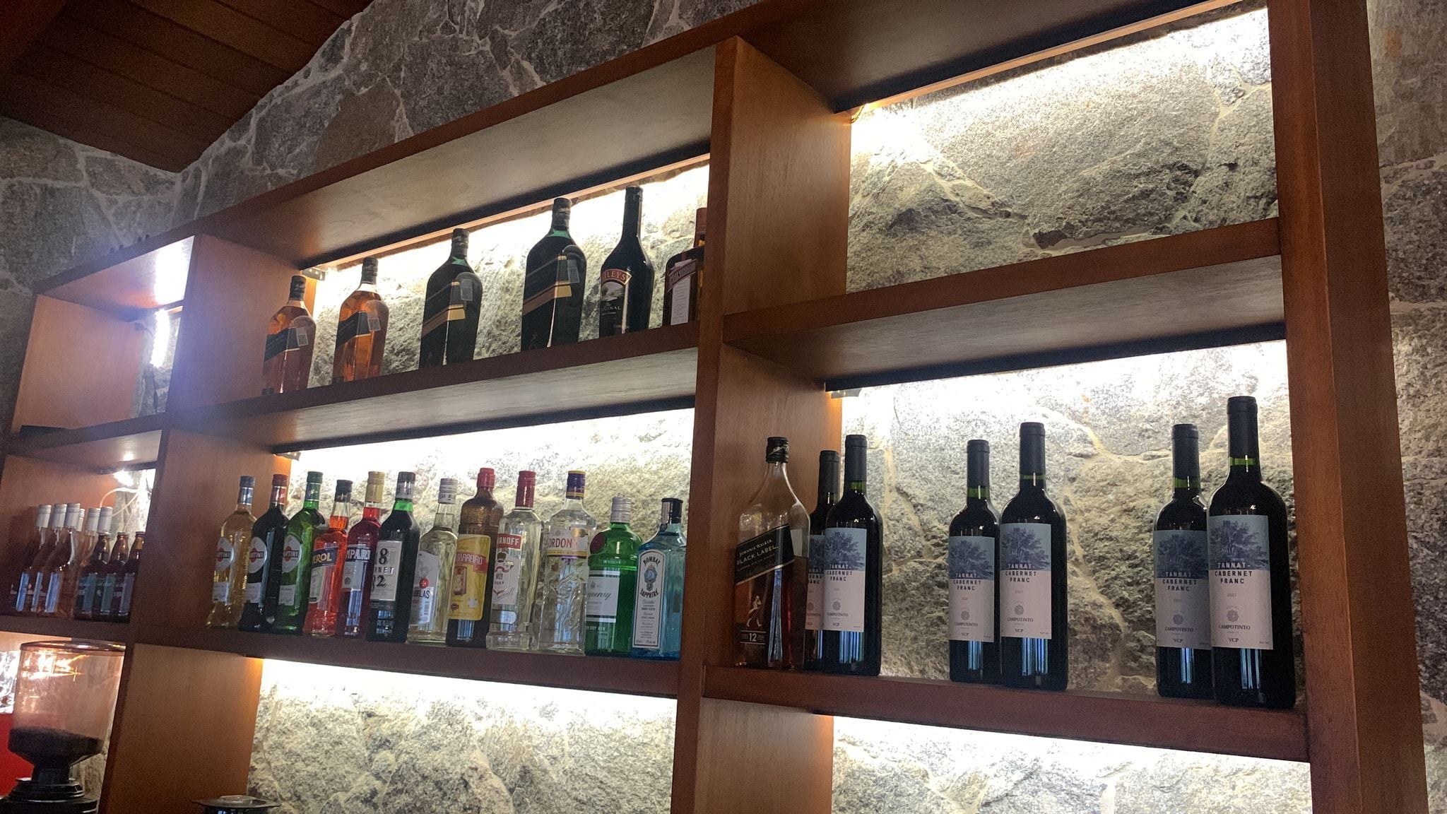 A wine rack with various bottles of wine, including Cabernet Franc and other varieties, in a rustic setting with stone walls.