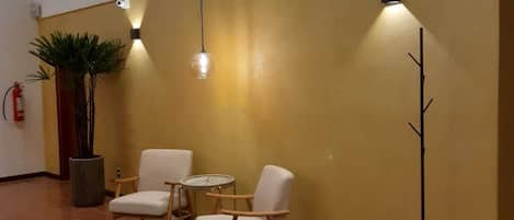 A modern interior with two white armchairs and a small round table, a large potted plant, and a tall floor lamp.