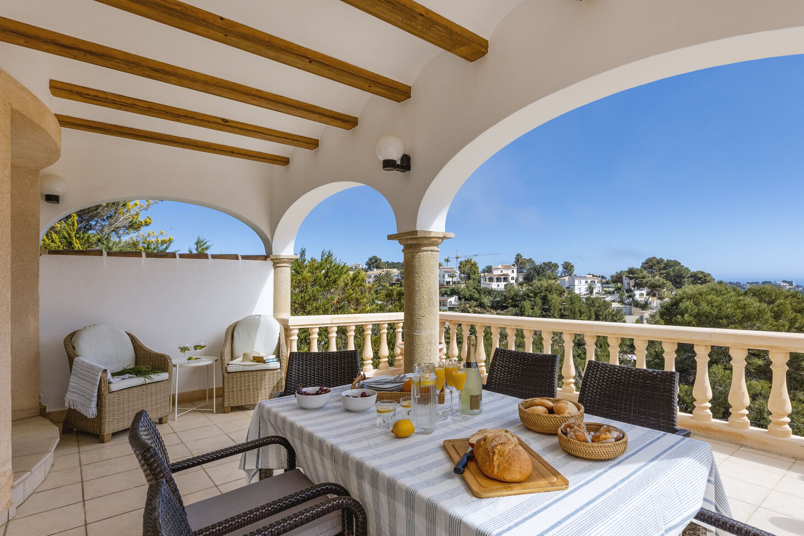 Una terraza con una mesa lista para el desayuno, mobiliario de mimbre y vistas al pueblo.