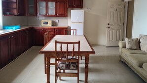 Cucina con mobili in legno, forno a microonde, frigorifero, tavolo da pranzo con sedie e divano in zona soggiorno.