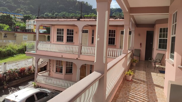 Un edificio a più piani con balconi, un patio piastrellato e vista su un pendio verde.