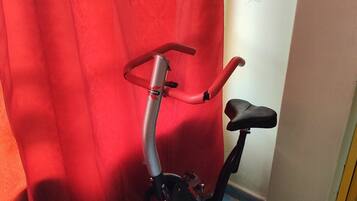 Een stilstaande trainingsfiets in een kamer met een rood gordijn en een vloer betegeld met blauw-witte patronen.
