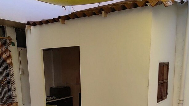 Una habitación con una mesa y sillas de vidrio, piso de baldosas, un toldo amarillo y una puerta que da a otra habitación.