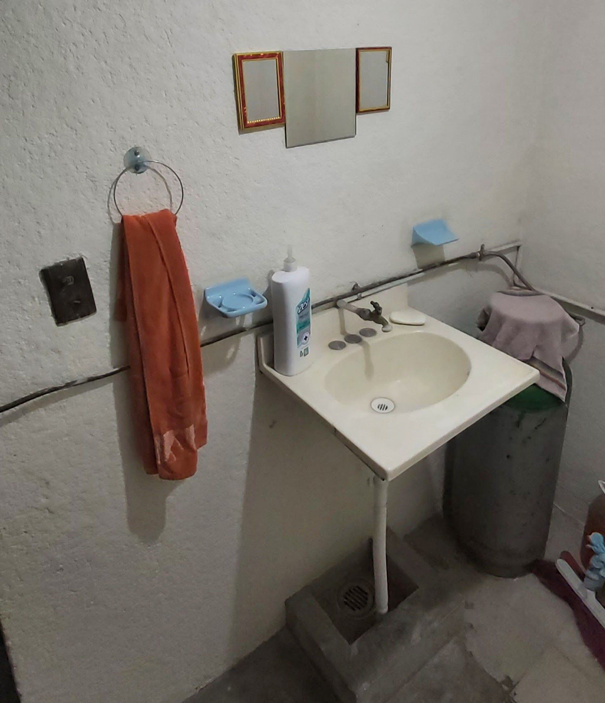 A small bathroom with a white sink, a mirror, a towel rack, a soap dispenser, and a trash can.