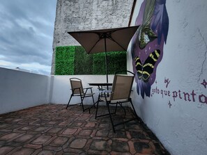 Relax in a serene outdoor space with a mural-adorned wall, comfortable seating, and a shaded area.