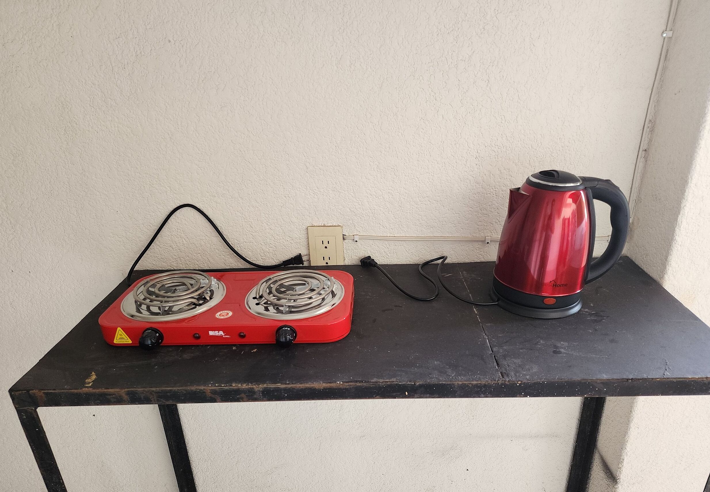 A red electric stove with two burners and a red electric kettle on a black table.