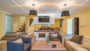 Una sala de estar moderna con televisión, sofás, una mesa de centro y una escalera que lleva a un comedor.