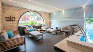 Un moderno espacio de spa con pared de piedra, un amplio ventanal arqueado y una piscina.