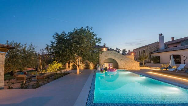 Una piscina con sillas de descanso y un arco de piedra al fondo.