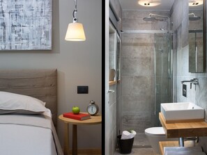 A modern bedroom with a bed, bedside table, and a lamp. Adjacent is a bathroom with a shower, sink, and toilet.