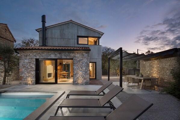 A modern house with a stone exterior, a swimming pool, and outdoor seating.