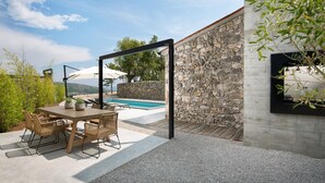 Ett poolområde med en stenmur, utemöbler och en pergola med parasoller.