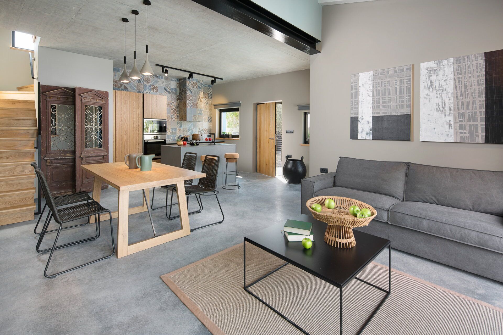 Un salon moderne avec un canapé gris, une table à manger en bois avec des chaises, et une table basse sur laquelle se trouve un panier de pommes.