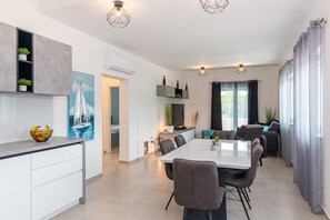 A modern kitchen with white cabinets, a dining area with a large table and chairs, and a living area with a sofa and curtains. - Villa Samba with Pool (Pula)