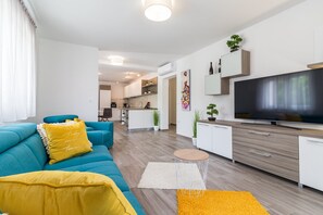 A modern living room with a sofa, a coffee table, a TV, and a kitchen in the background. - Villa Samba with Pool (Pula)