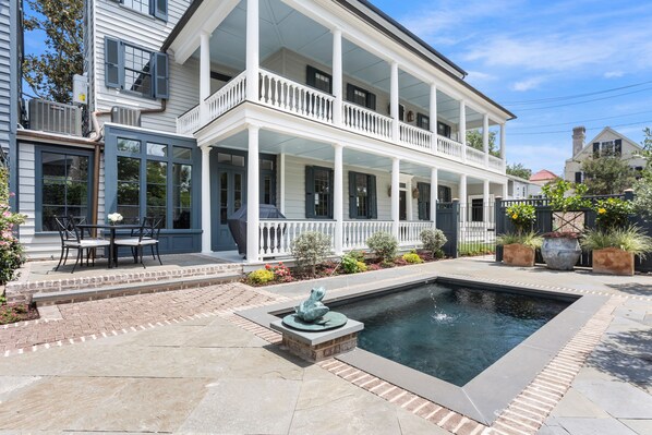 A two-story house with a covered porch, a swimming pool, and outdoor seating.