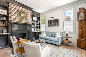A living room with a fireplace, a blue sofa, a round coffee table, and a large clock.