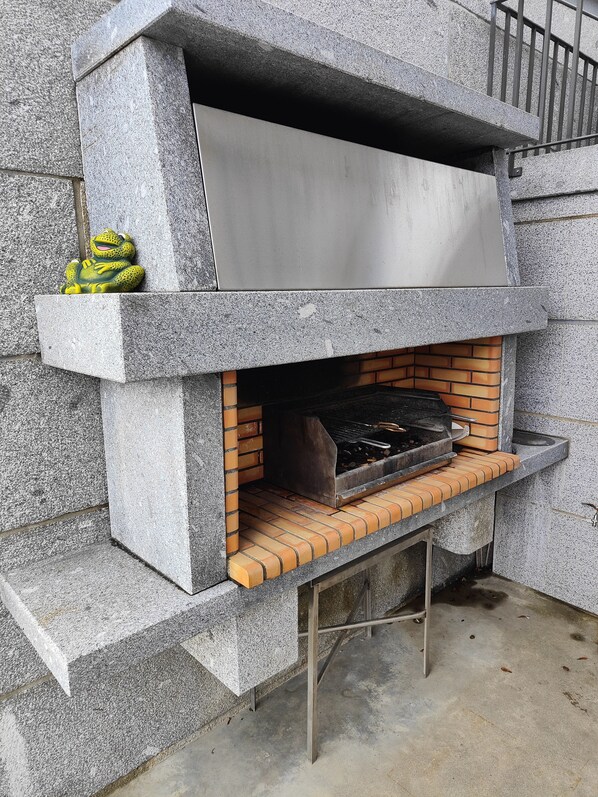 A stone-built outdoor grill with a metal hood and a brick base.