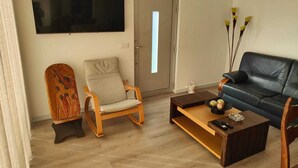 Un soggiorno con pavimento in legno, un divano in pelle nera, una poltrona in legno, un tavolino da caffè e un televisore piatto montato a parete.