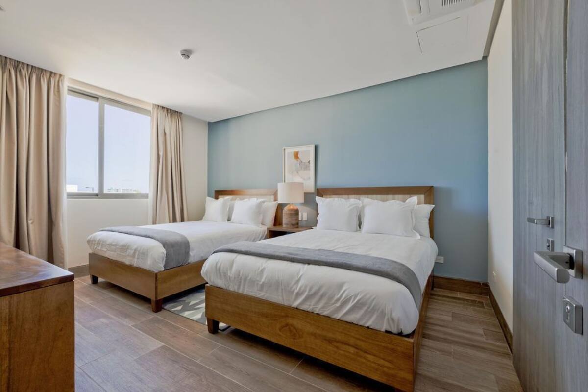 A hotel room with two beds, a desk, and a window with curtains.