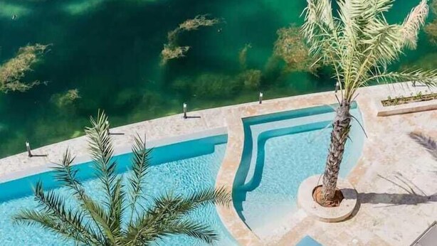 Vista aérea de una piscina en un complejo turístico, con tumbonas y palmeras.