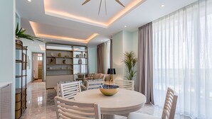 Un comedor moderno con una mesa redonda, sillas blancas y un bol en el centro. Se observa una estantería al fondo y un ventanal con cortinas.
