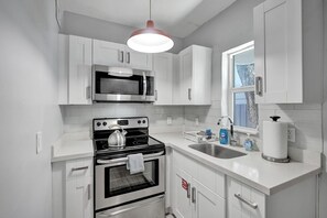 A kitchen with white cabinets, a stainless steel microwave, a stove, and a sink.