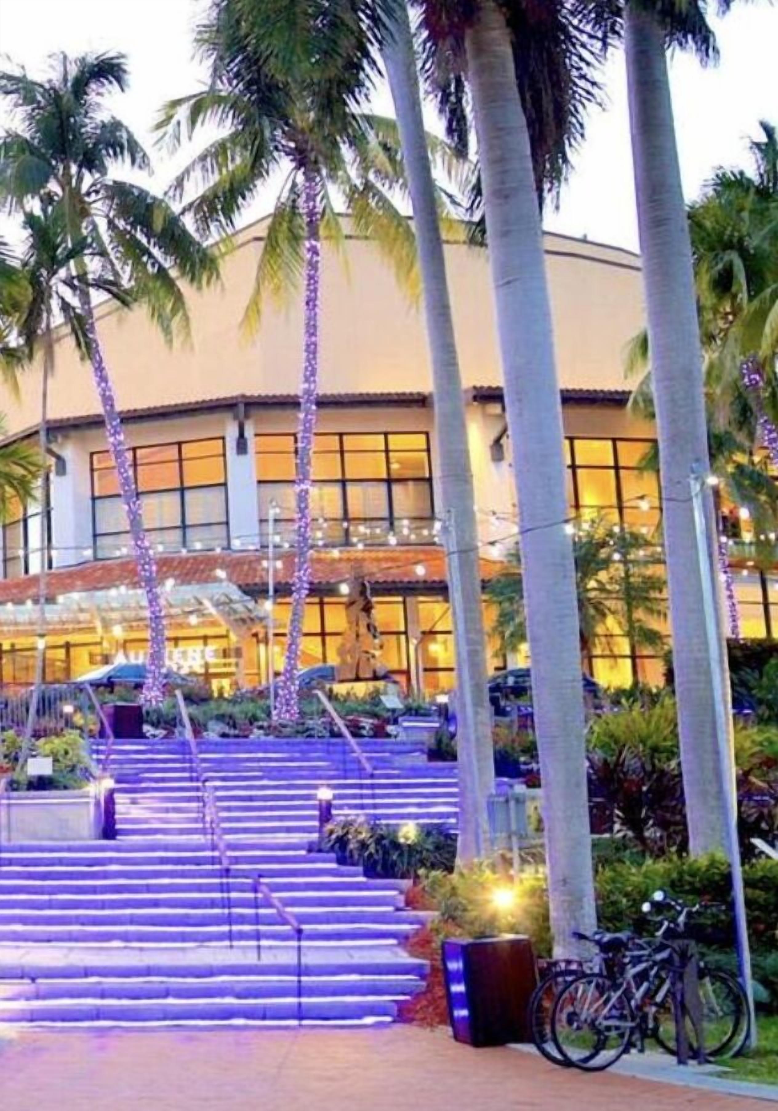 A hotel entrance with a staircase, palm trees, and a building with large windows.