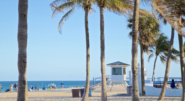 A beach with palm trees, a lifeguard tower, and people on the sand.