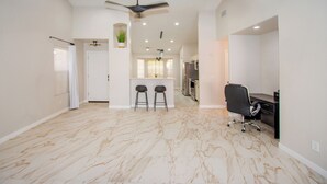 A spacious living area with a marble floor, a ceiling fan, a kitchen area with a dining set, and a black office chair.