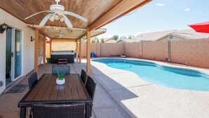 A covered patio area with a pool, outdoor furniture, and a ceiling fan.