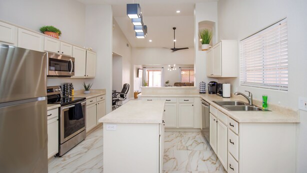 A modern kitchen with white cabinets, stainless steel appliances, a marble floor, and a central island.